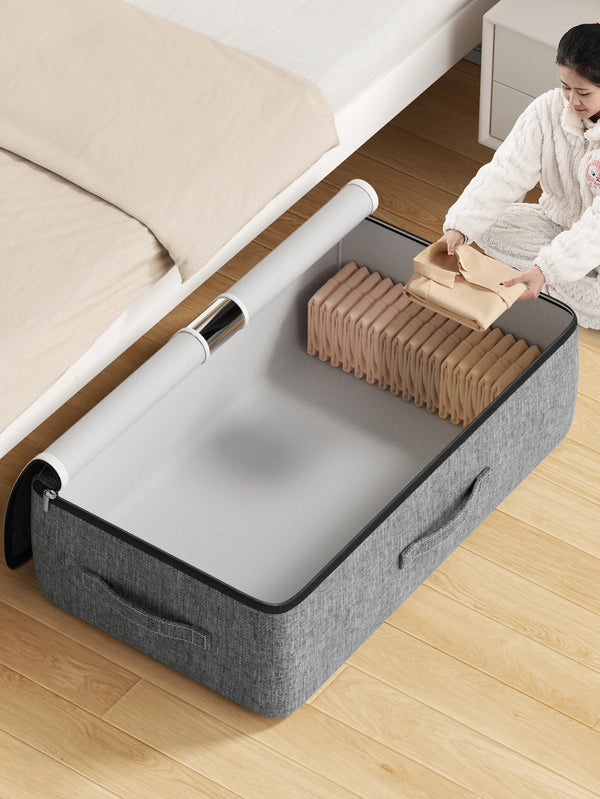Open grey under-bed storage bag being filled with folded clothes